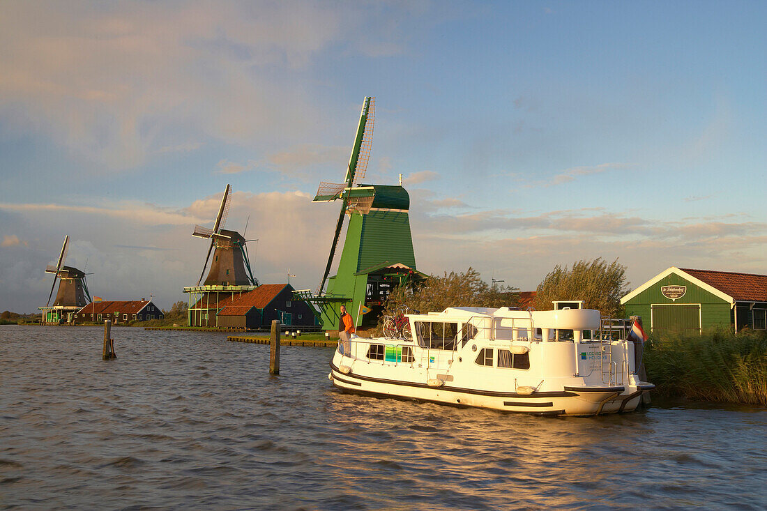 A boat and windmills in the light of the setting sun, Open-air museum Zaanseschans at the river Zaan, Netherlands, Europe