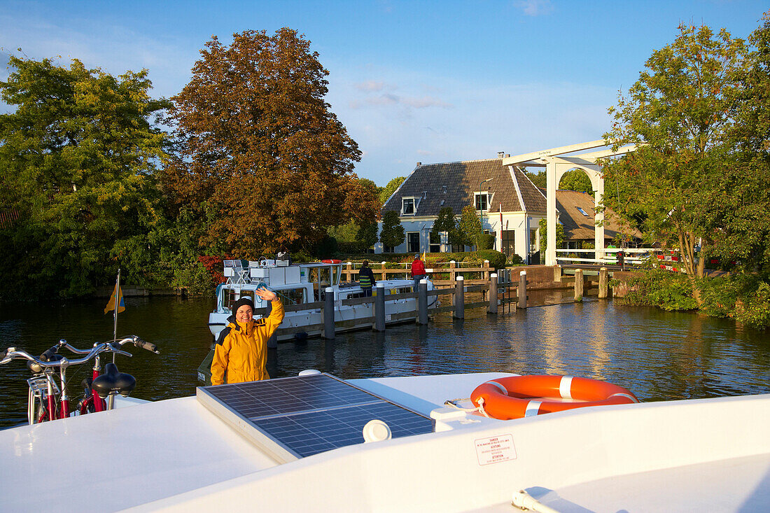 Waving woman on a houseboat on the river Vecht, bascule bridge in the background, Netherlands, Europe
