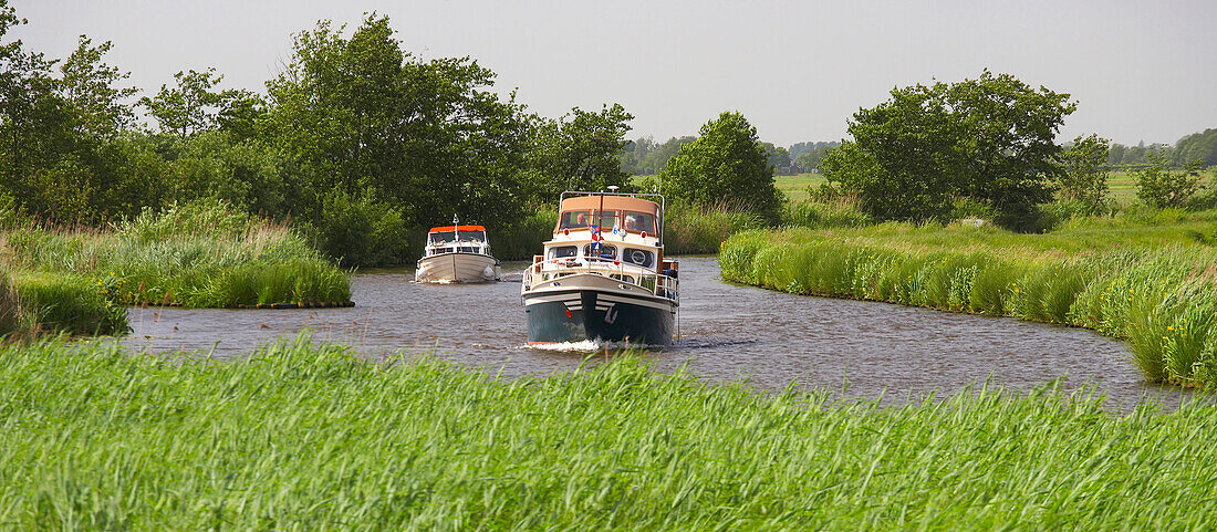 Two houseboats driving on the river Grecht under grey sky, Netherlands, Europe