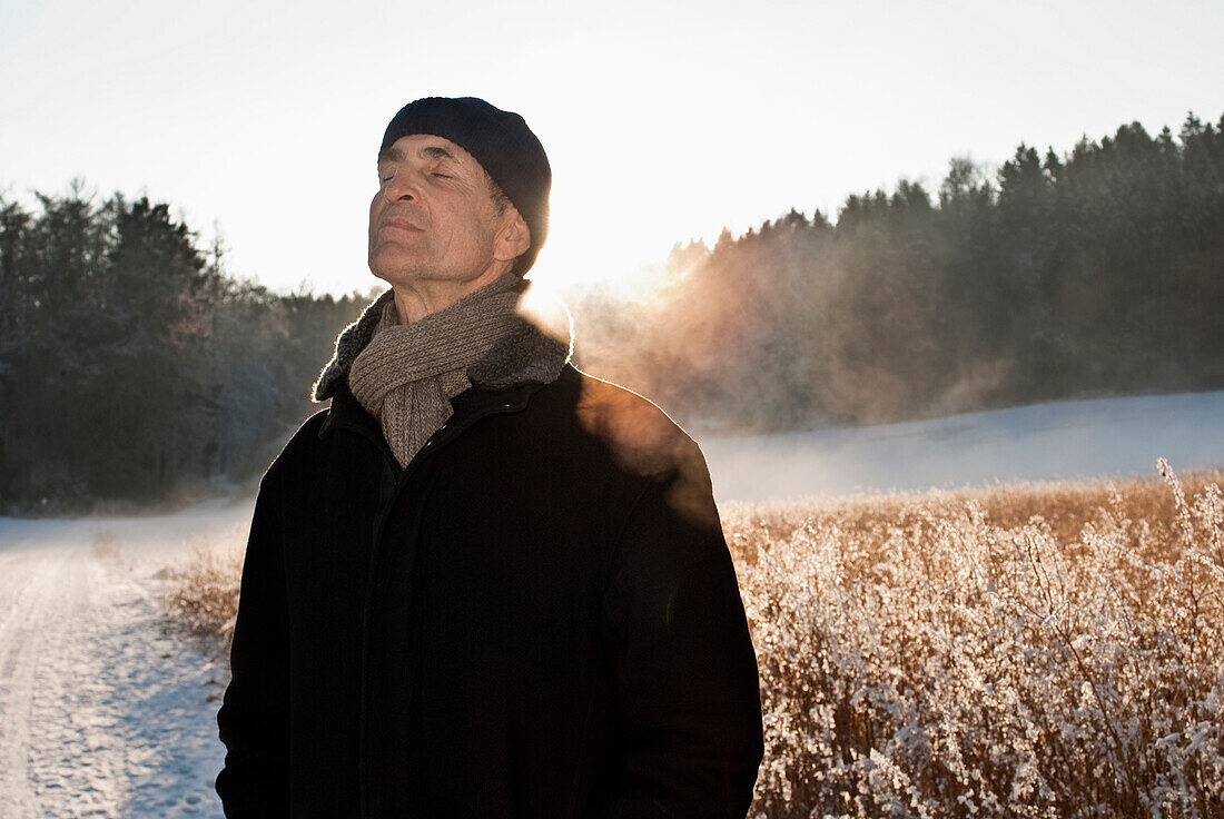 Alter Mann steht mit geschlossenen Augen in einer Winterlandschaft, Windach, Oberbayern, Deutschland