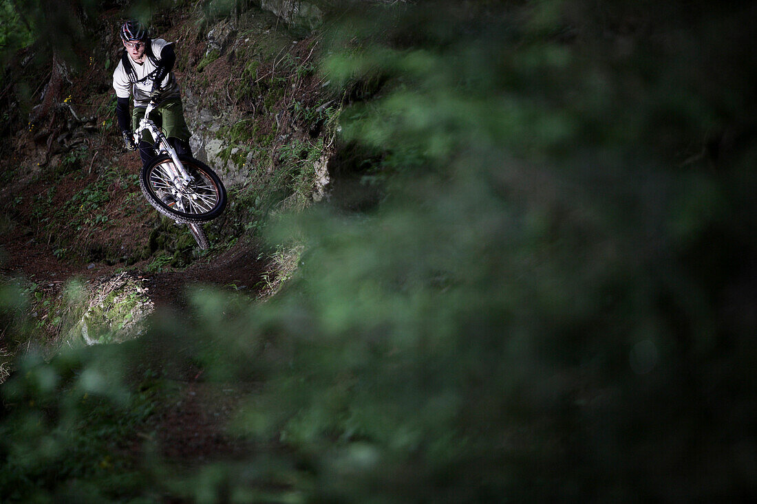 Mountainbiker springt im Wald, Ischgl, Tirol, Österreich