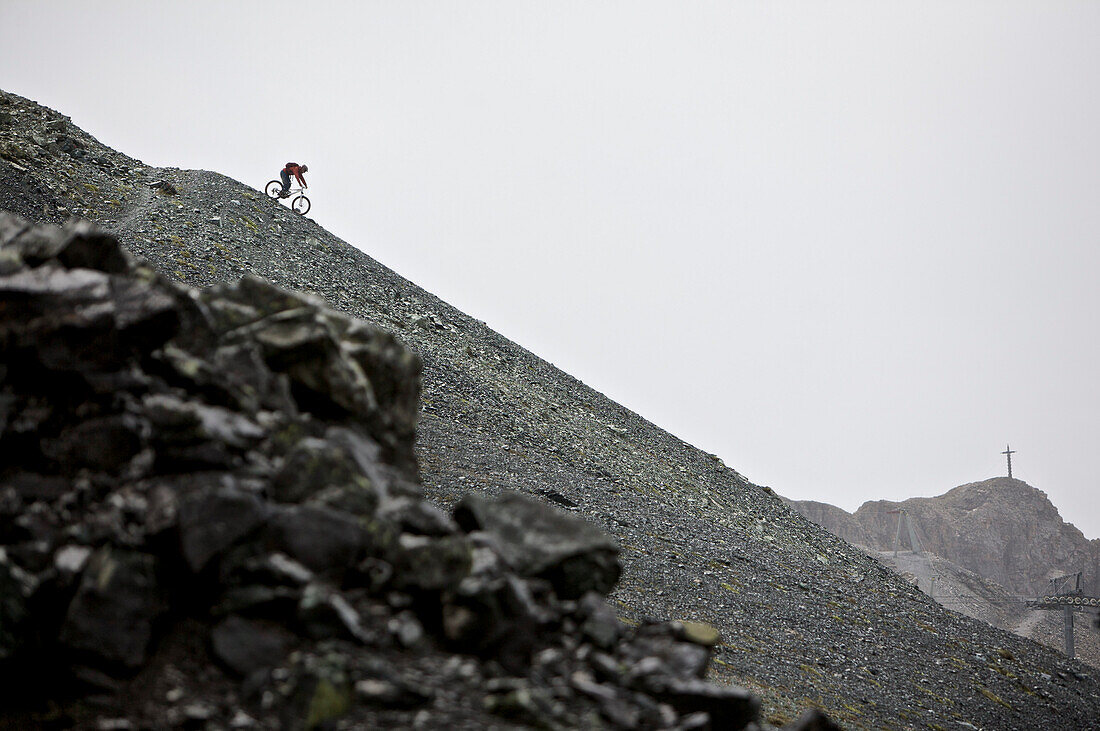 Mountainbiker fährt eine Geröllhalde in den Bergen hinunter, Ischgl, Tirol, Österreich