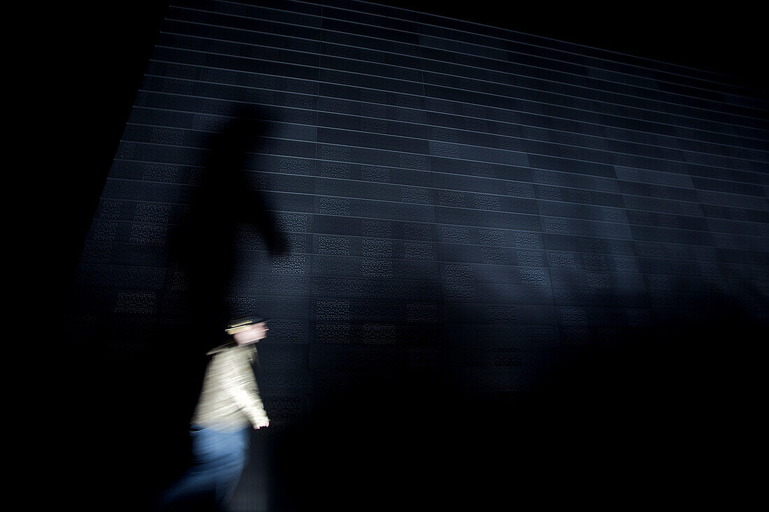Person walking past a wall at night, Oslo, Norway