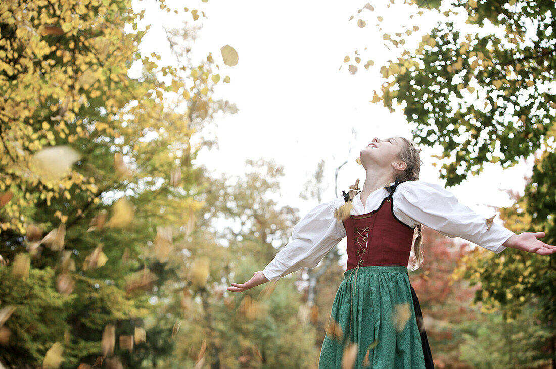 A girl wearing a Dirndl dress playing with leaves, Kaufbeuren, Bavaria, Germany
