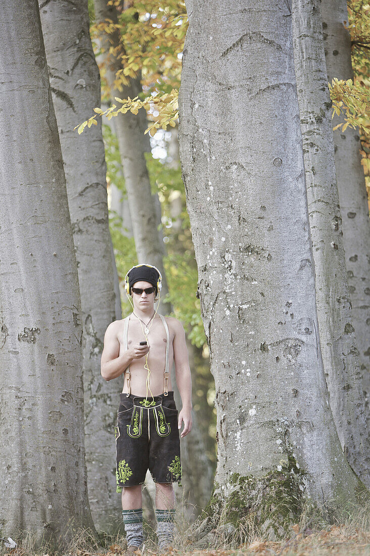 Young man wearing leather trousers standing in a forest, Kaufbeuren, Bavaria, Germany
