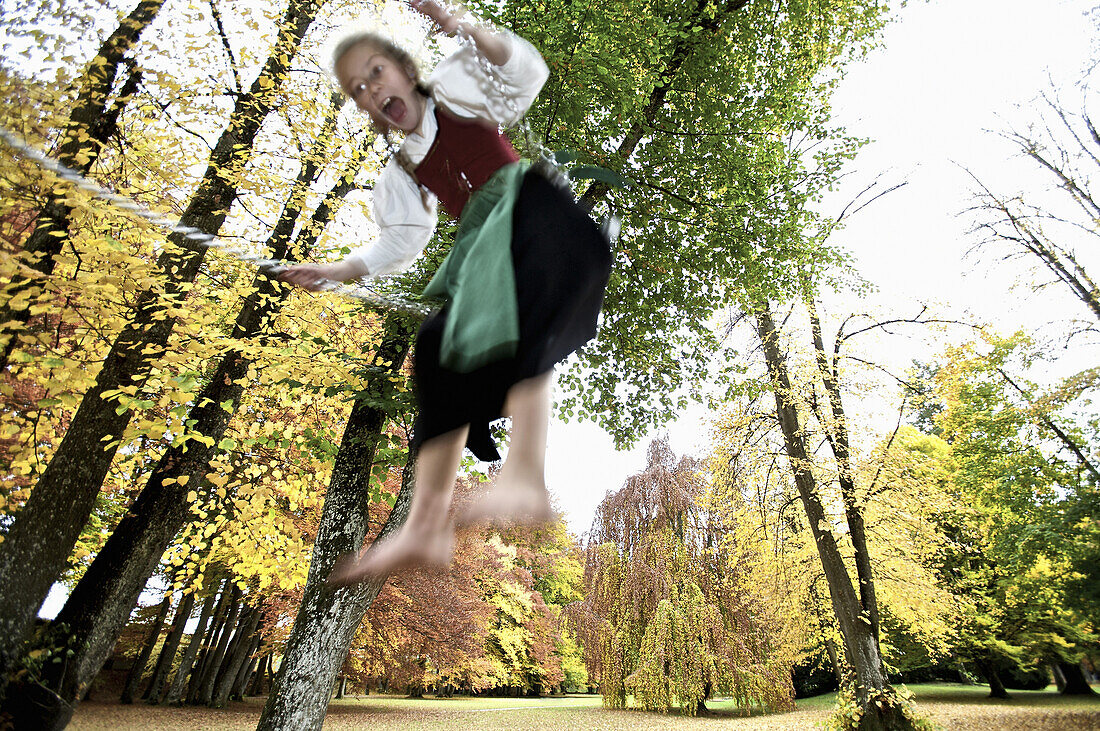 Girl wearing a dirndl, swinging in a park, Kaufbeuren, Bavaria, Germany