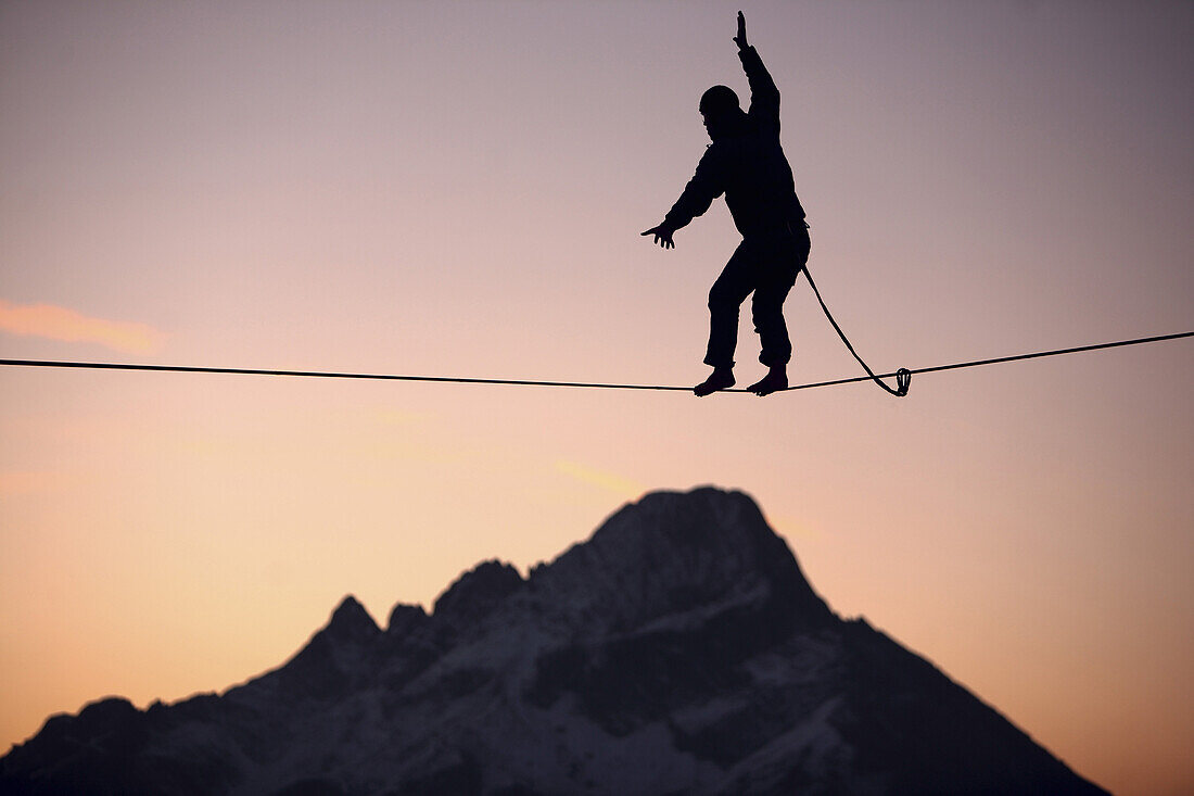 Mann balanciert auf einer Slackline im Sonnenaufgang, Oberstdorf, Bayern, Deutschland