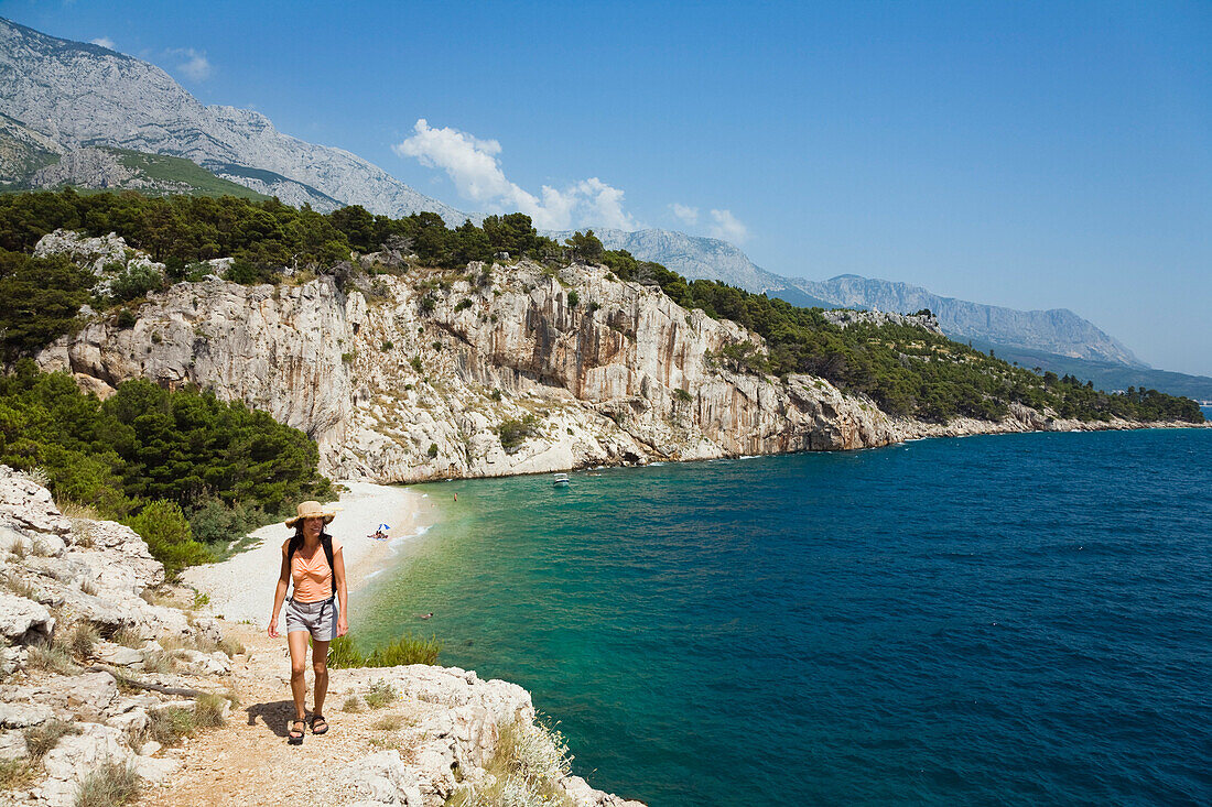 Eine Frau geht auf einem Küstenweg im Sonnenlicht, Nudal Beach, Dalmatien, Kroatien, Europa