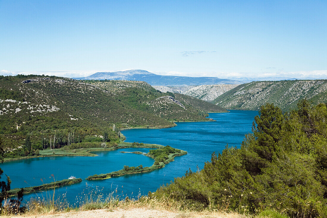 Der Fluss Krka und Berglandschaft unter blauem Himmel, Krka Nationalpark, Dalmatien, Kroatien, Europa