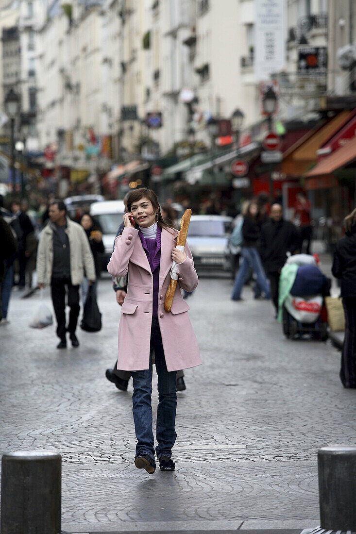 A young woman holding a baguette and talking on her cell phone on the street of Paris. Paris. France