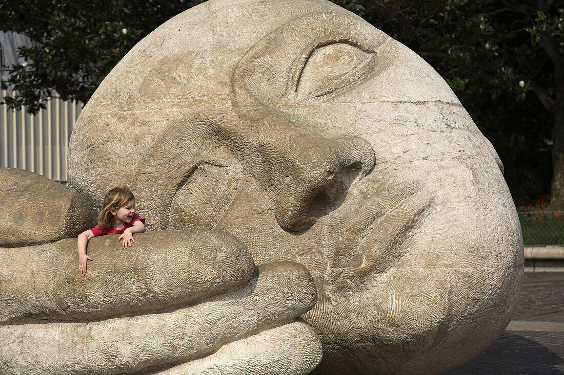 A young girl playing on the sculptured head I'Ecoute in front of St-Eustache Church. Paris. France
