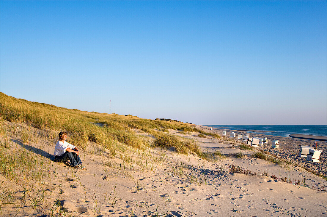 Frau sitzt in einer Düne, Rantum, Sylt, Nordfriesland, Schleswig-Holstein, Deutschland
