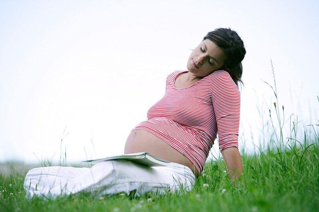 Schwangere Frau sitzt auf einer Wiese und ruht sich aus