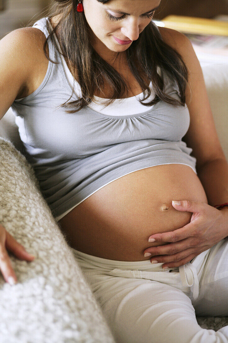 Schwangere Frau sitzt auf einem Sofa und berührt ihren Bauch