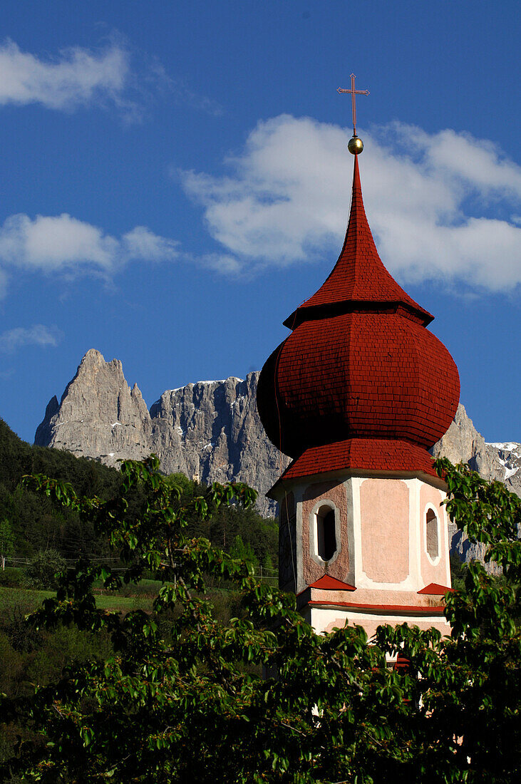 Der Kirchturm der St. Oswald Kirche zwischen grünen Zweigen und Bergen, Kastelruth, Südtirol, Italien, Europa
