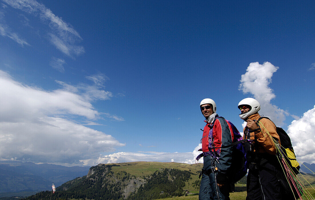 Two men wearing helmets in front of mountains and blue sky, Alpe di Siusi, Valle Isarco, South Tyrol, Italy, Europe