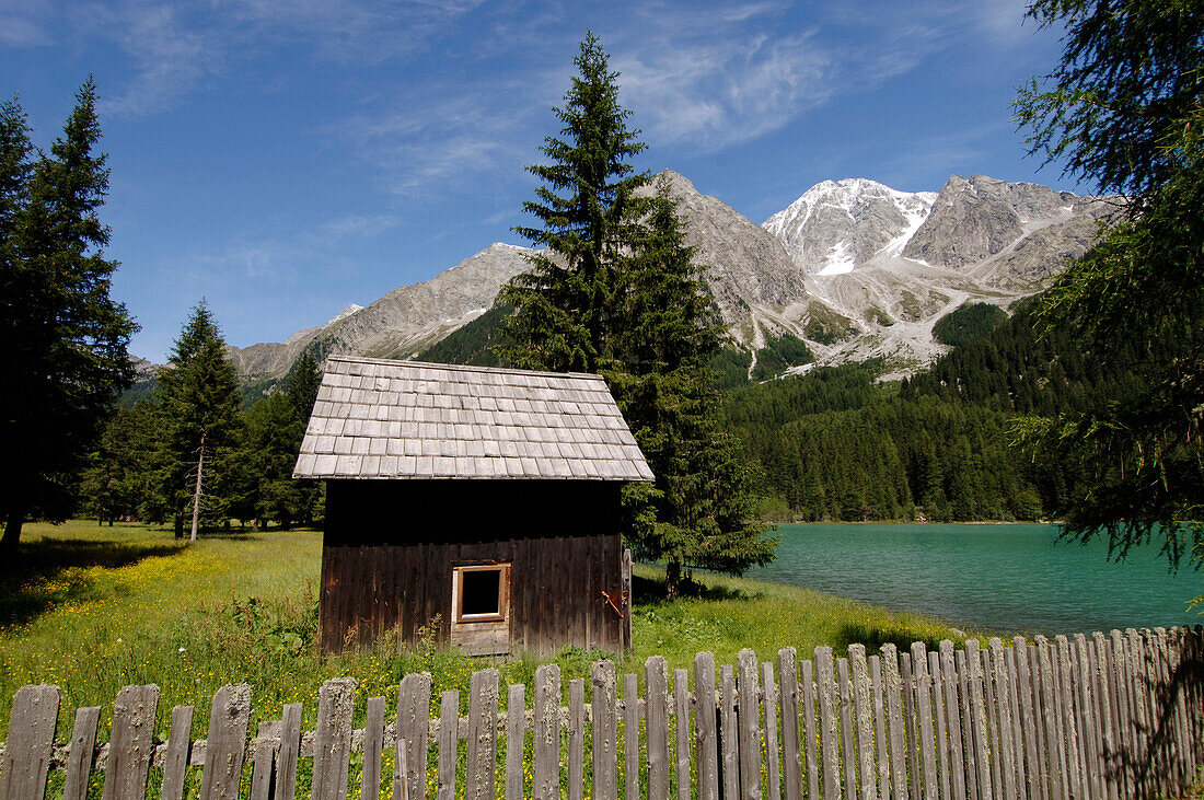 Holzhütte und Zaun am Antholzersee in idyllischer Berglandschaft im Sonnenlicht, Pustertal, Südtirol, Italien, Europa