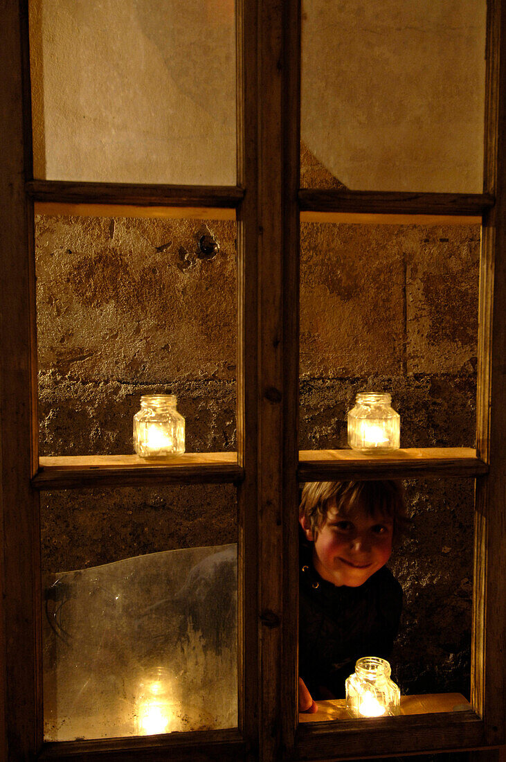 A boy looking through a candle-lit window at the christmas market, Glurns, Val Venosta, South Tyrol, Italy, Europe