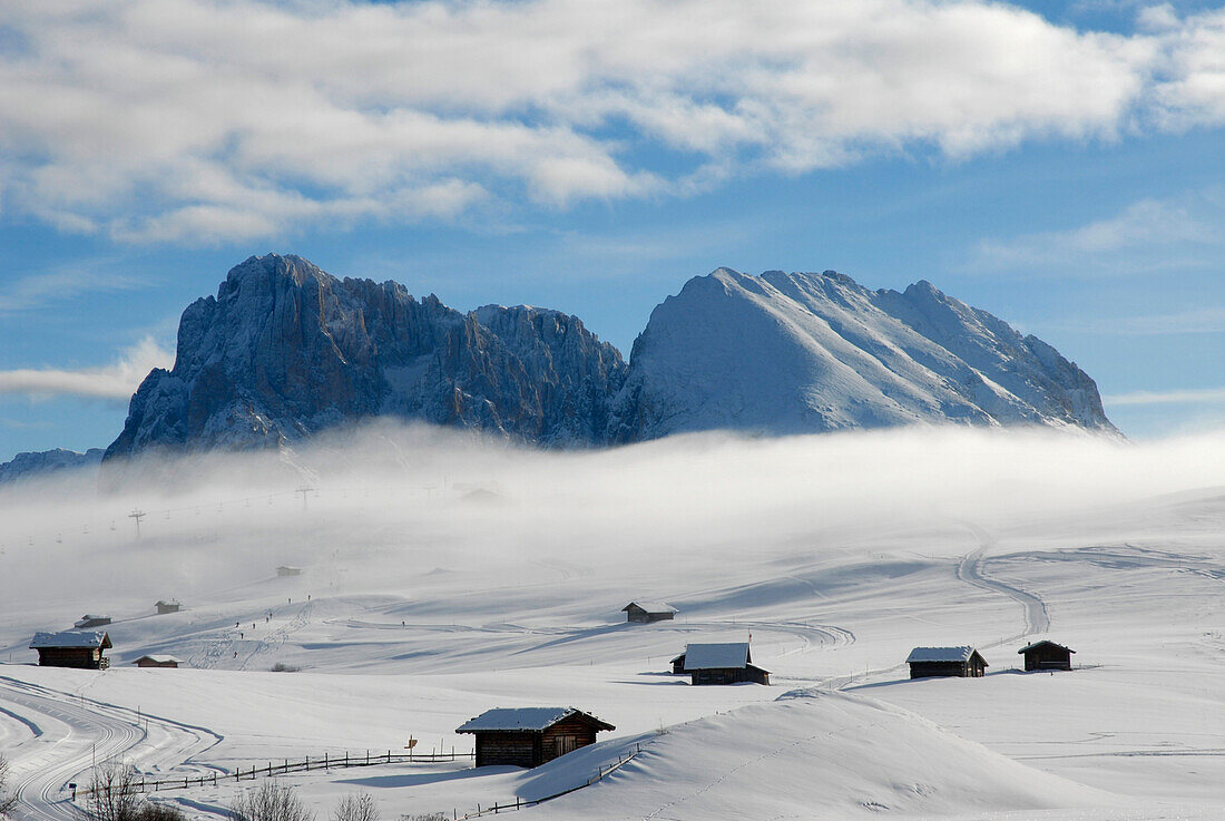 Wafts of mist over winter landscape with alpine huts, Alpe di Siusi, South Tyrol, Italy, Europe