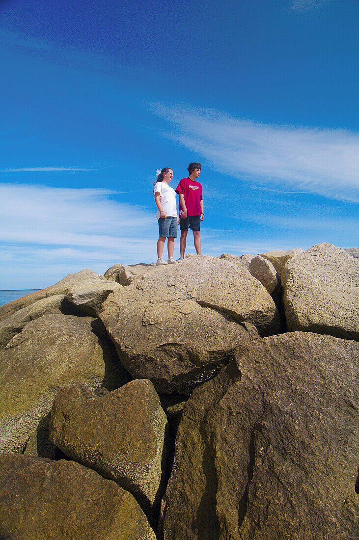 12 year old girl and her 15 year old brother standing on the rocks at Rock Harbor, Orleans, Cape Cod, Massachusetts, USA