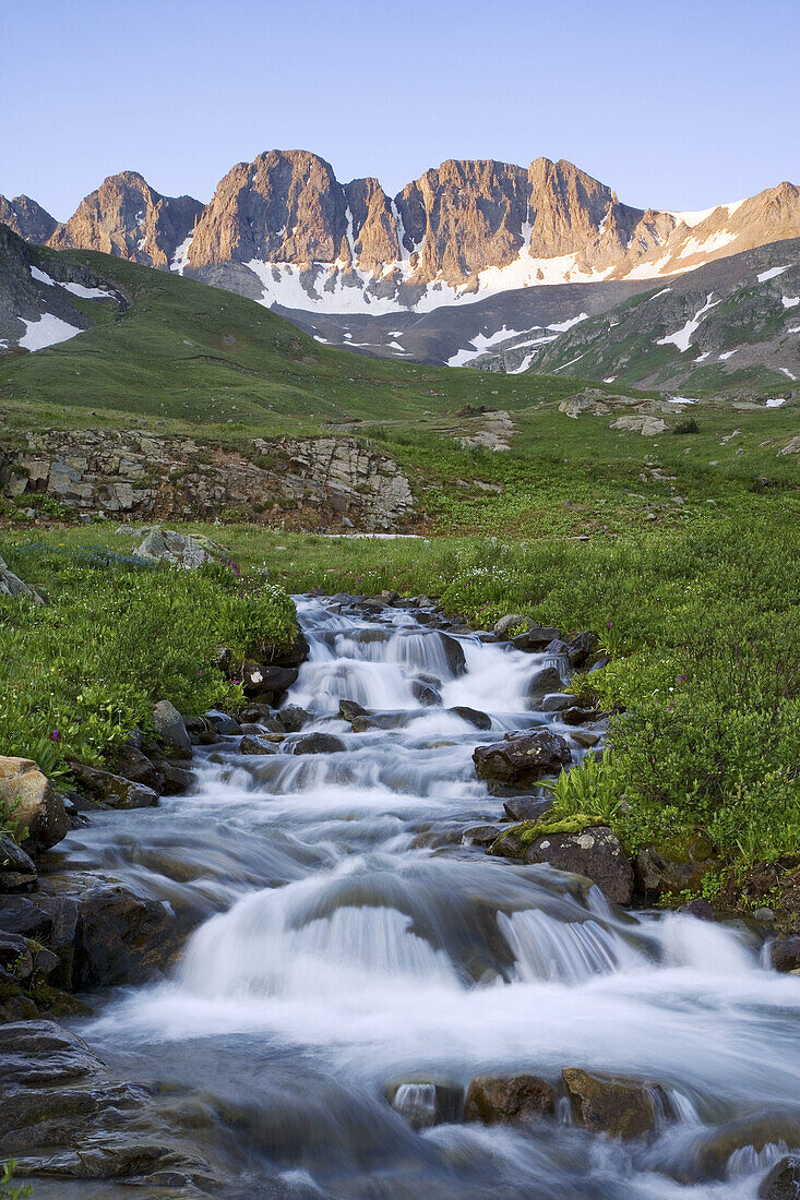 Alpenglow on peaks above American Basin with an unnamed creek rushing through green meadows, San Juan Mountains, Colorado, USA