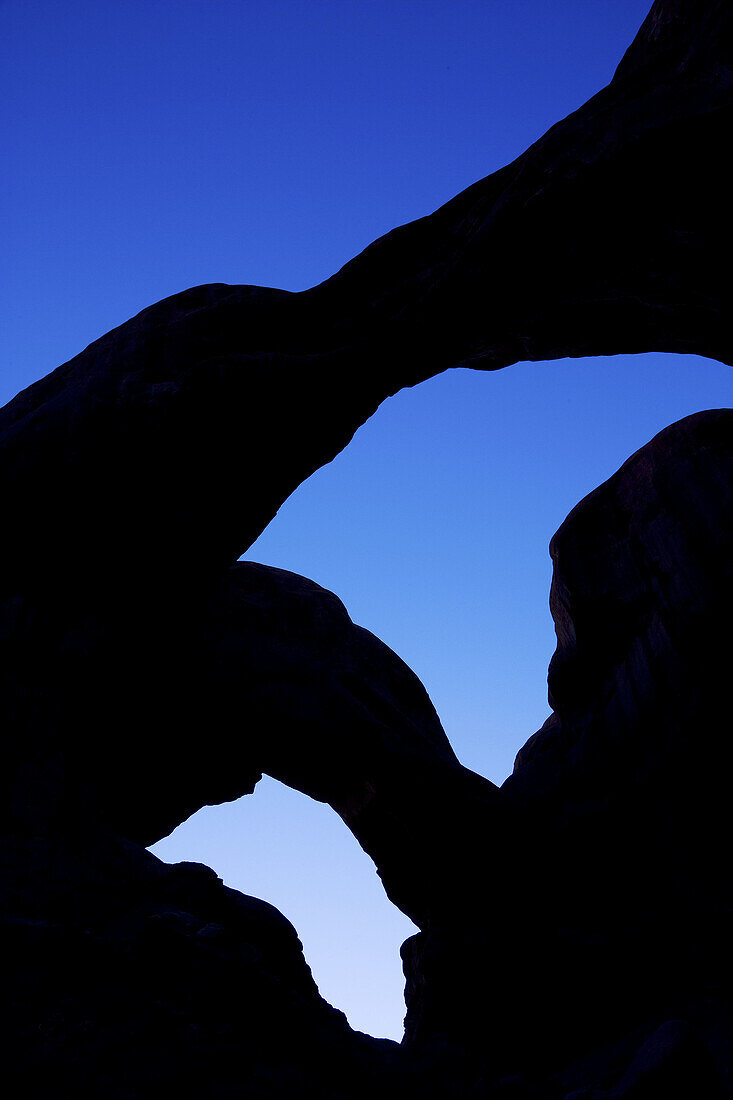 Double Arch in silhouette against a deep blue evening sky, Arches National Park, Utah, USA