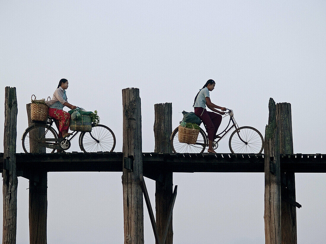 Burmese girls riding bikes on the U Bein teak bridge in Myanmar