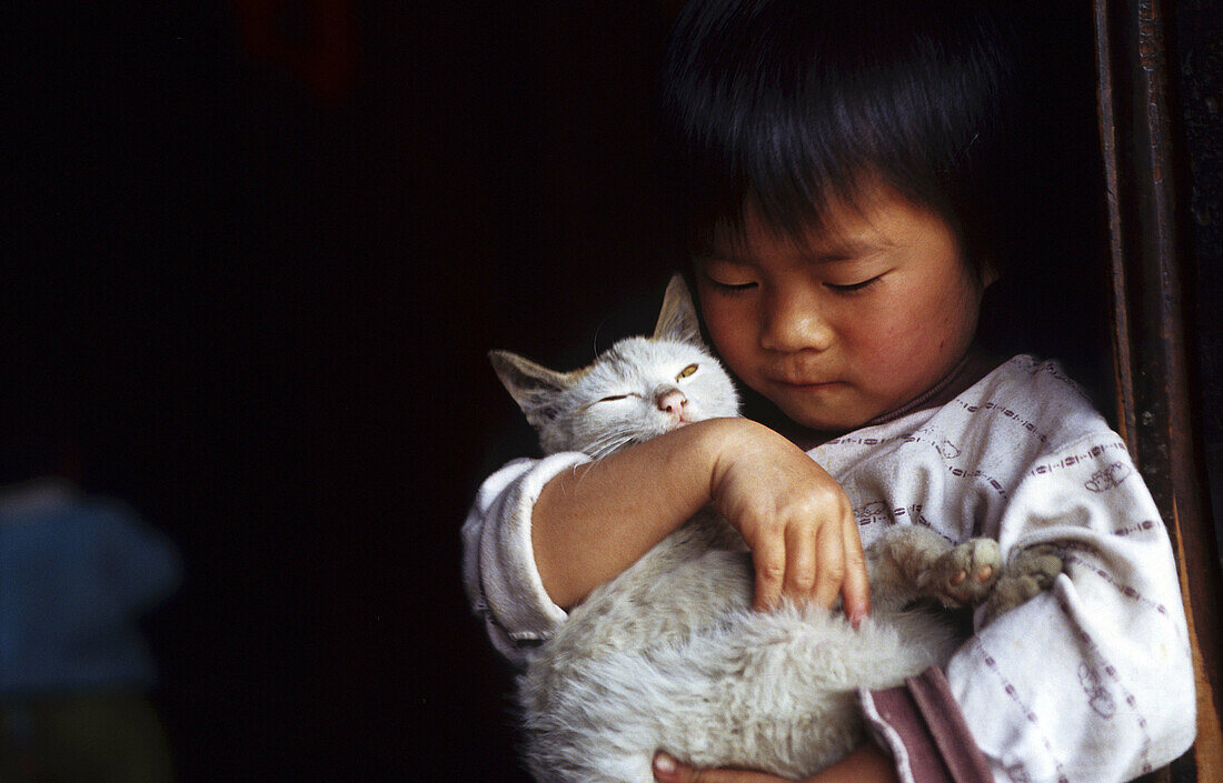 A little girl from the Miao minority holds her sweet cat, China