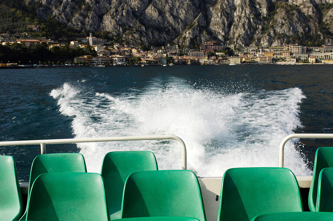 Blick über die Stühle eines Ausflugsboots auf die Stadt Limone, Gardasee, Italien, Europa