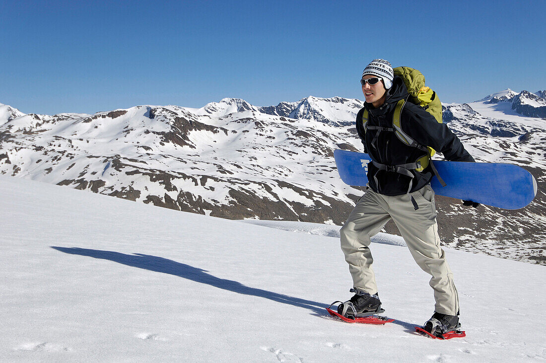 Snowboarder mit Snowboard beim Aufstieg unter blauem Himmel, Schnalstal, Vinschgau, Südtirol, Italien, Europa