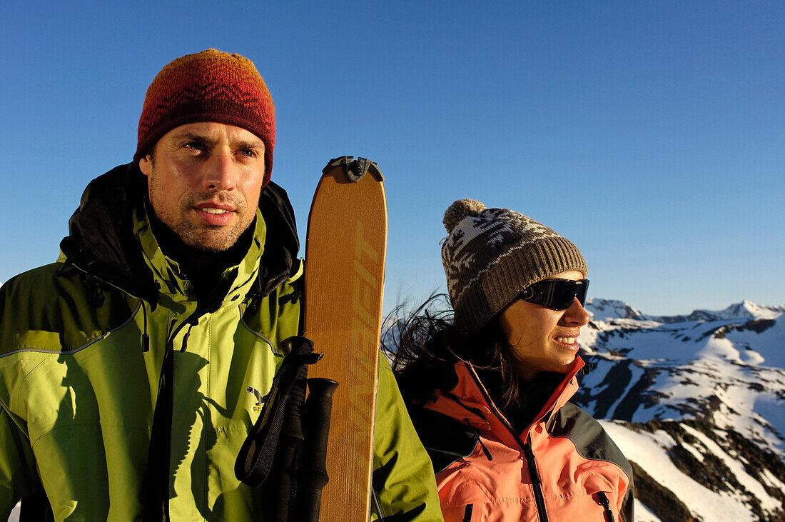 Mann und Frau mit Ski vor verschneiten Bergen im Sonnenlicht, Schnalstal, Vinschgau, Südtirol, Italien, Europa