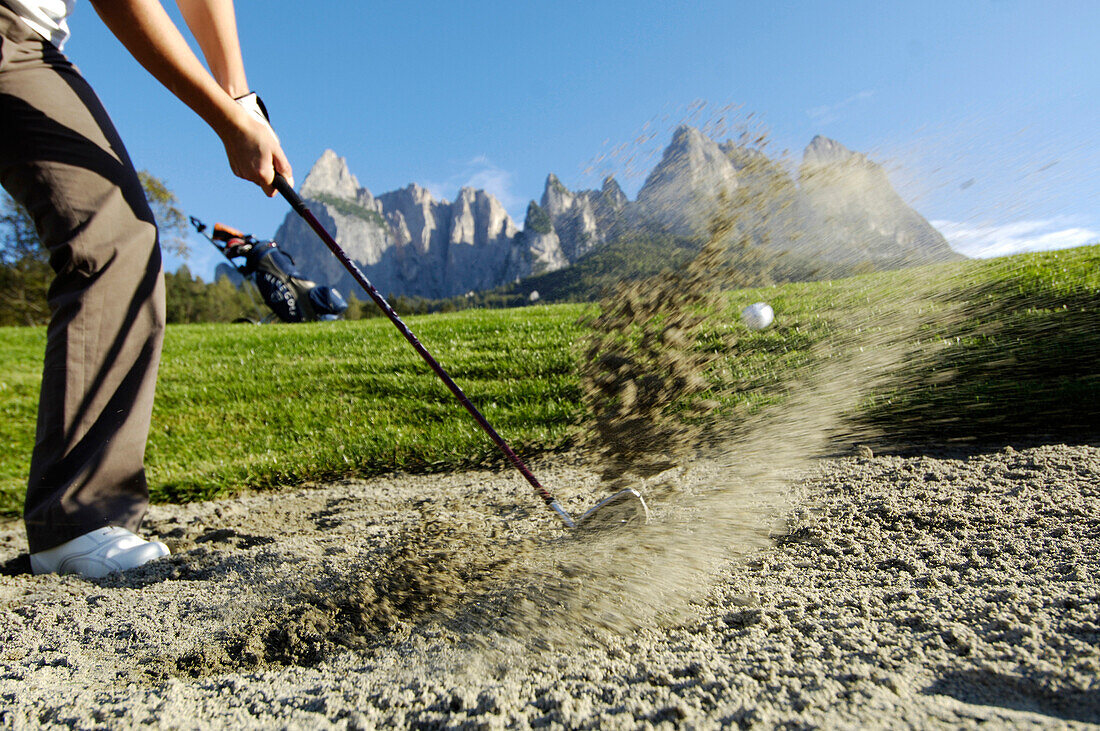 A woman hitting the golf ball out of the bunker, golf court Kastelruth Alpe di Siusi, Sciliar, South Tyrol, Italy, Europe