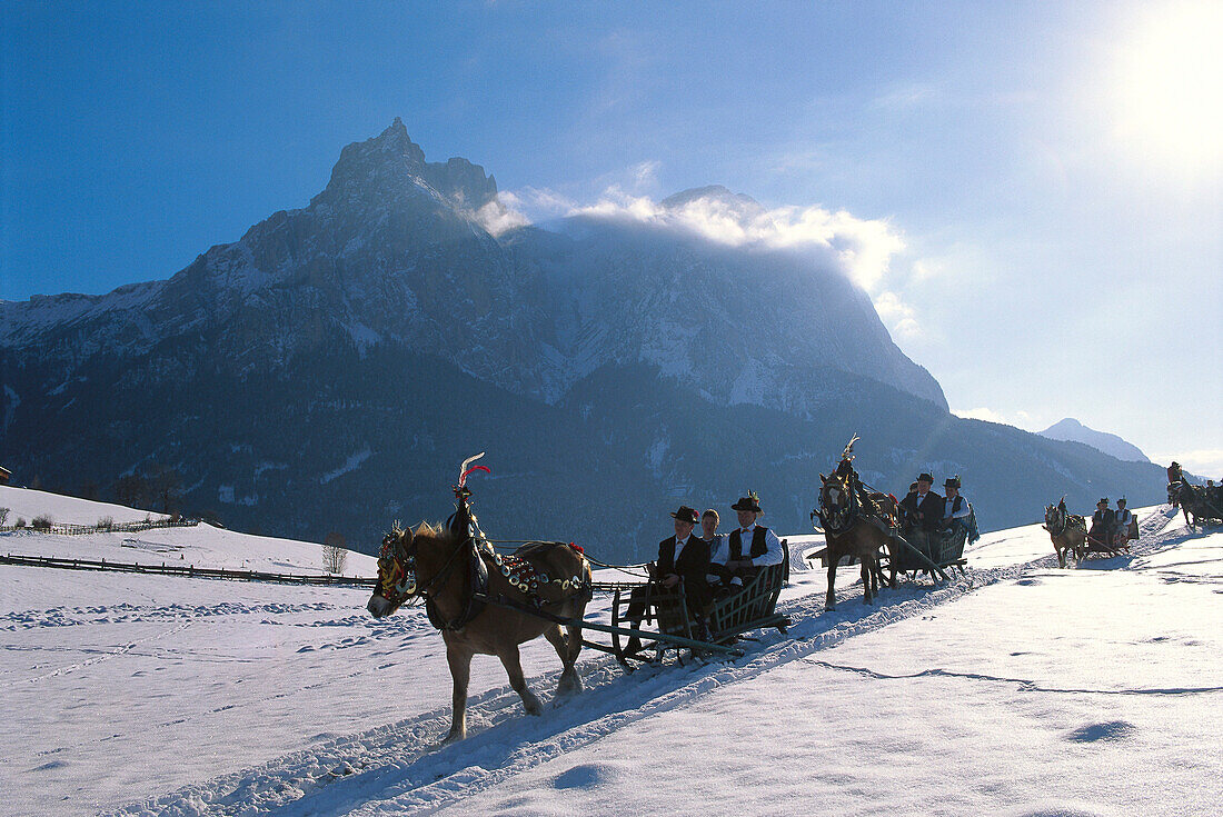 Menschen in Tracht fahren mit Pferdeschlitten durch sonnige Winterlandschaft, Schlern, Südtirol, Italien, Europa