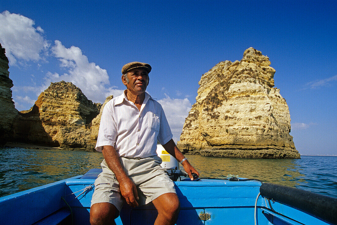 Mature man at the rudder of a boat under blue sky, Ponta da Piedade, Algarve, Portugal, Europe