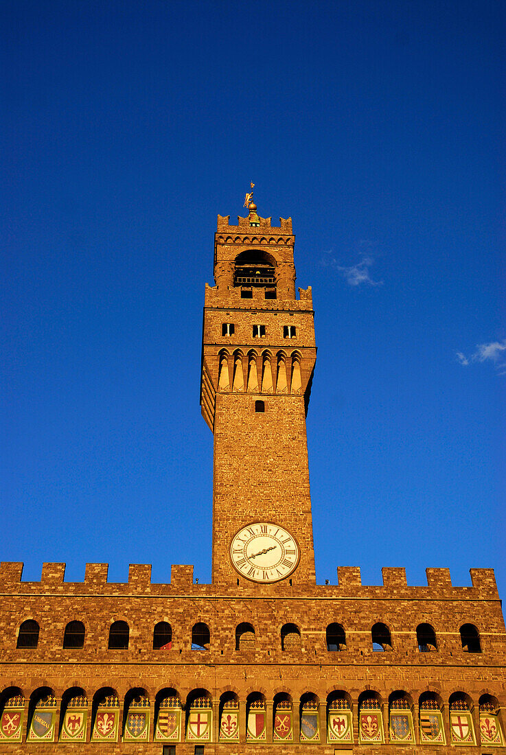 Palazzo Vecchio, tower with clock and emblems under blue sky, Florence, Tuscany, Italy, Europe