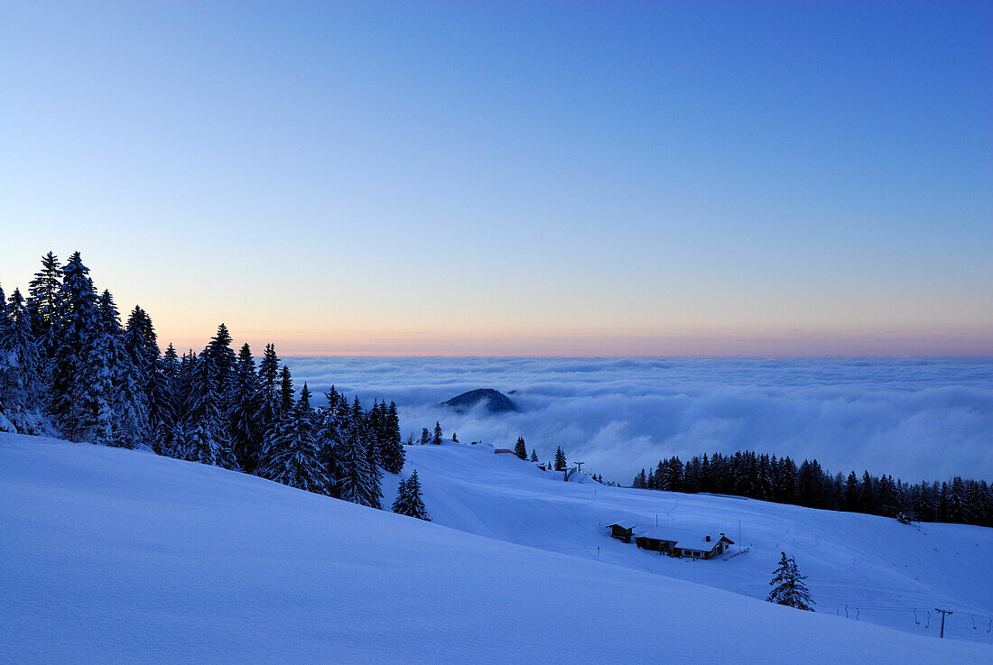 Snow-covered alpine hut above fog bank at dusk, Kampenwand, Chiemgau Alps, Chiemgau, Bavaria, Germany