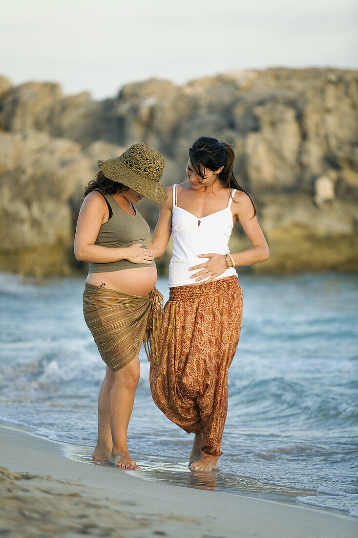 Two female friends, one woman is pregnant, walking along the beach