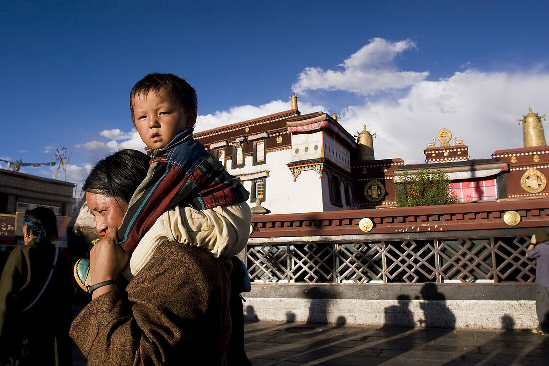 Mom carrying son around the Jokhang temple Kora (pilgrimage circuit) in old Lhasa, Tibet, China