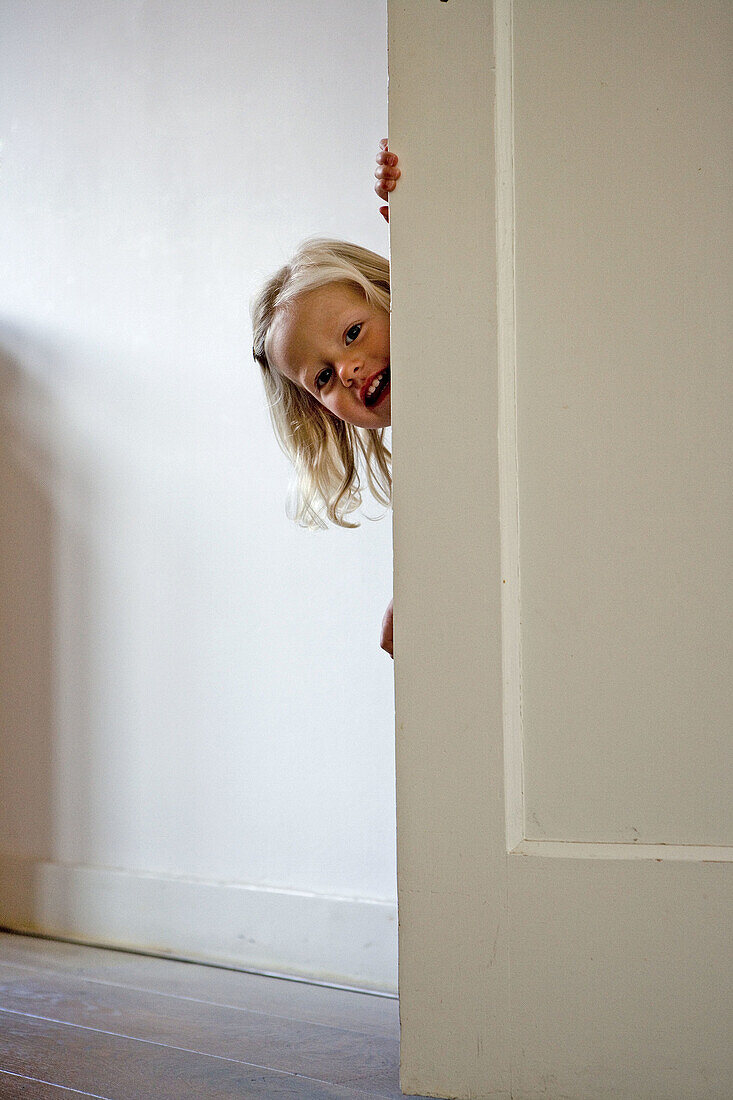 Blond little girl is hiding behind a door