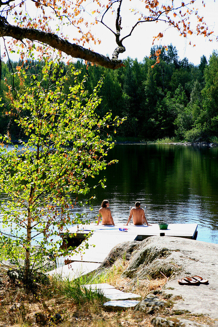 Menschen sitzen auf einem Holzsteg im Sonnenlicht, Saimaa Seenplatte, Finnland, Europa