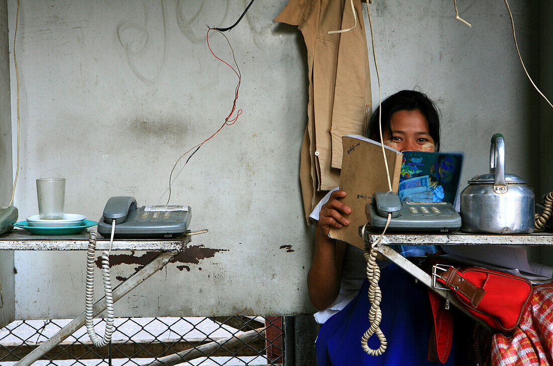 Lesende Frau sitzt hinter Telefonen, Möglichkeit zu telefonieren, Rangoon, Myanmar, Birma, Asien