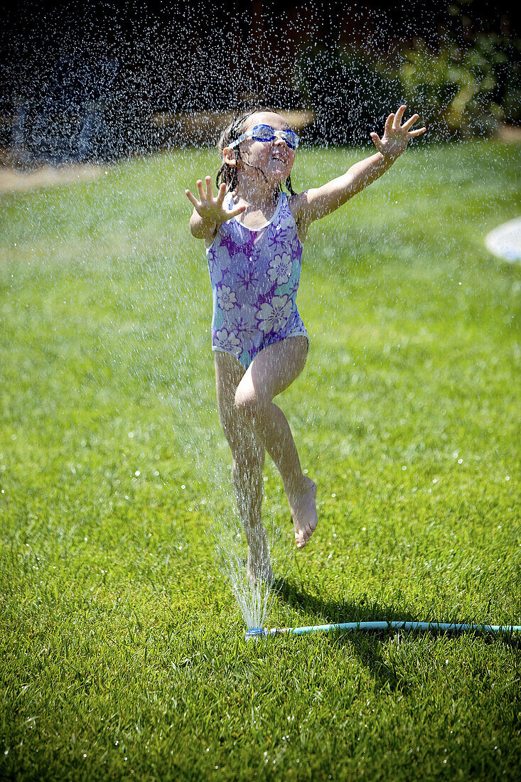 Young girl leaps through yard sprinkler