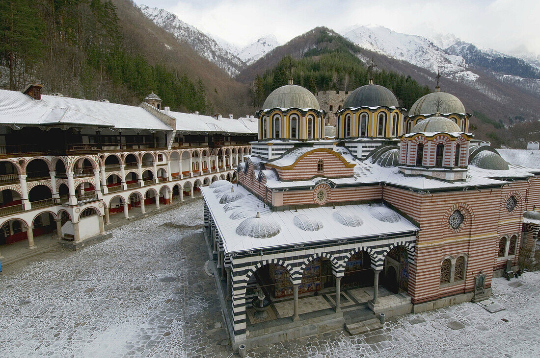 Rila monastery after snowfall, inner court, Mary`s Birth Church, residential building, snow-covered Rila mountains and surrounding forests, Bulgaria