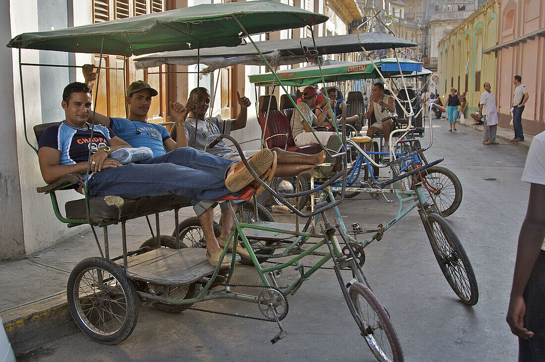 Bici-taxi drivers relaxing together on their machines, while waiting for customers.