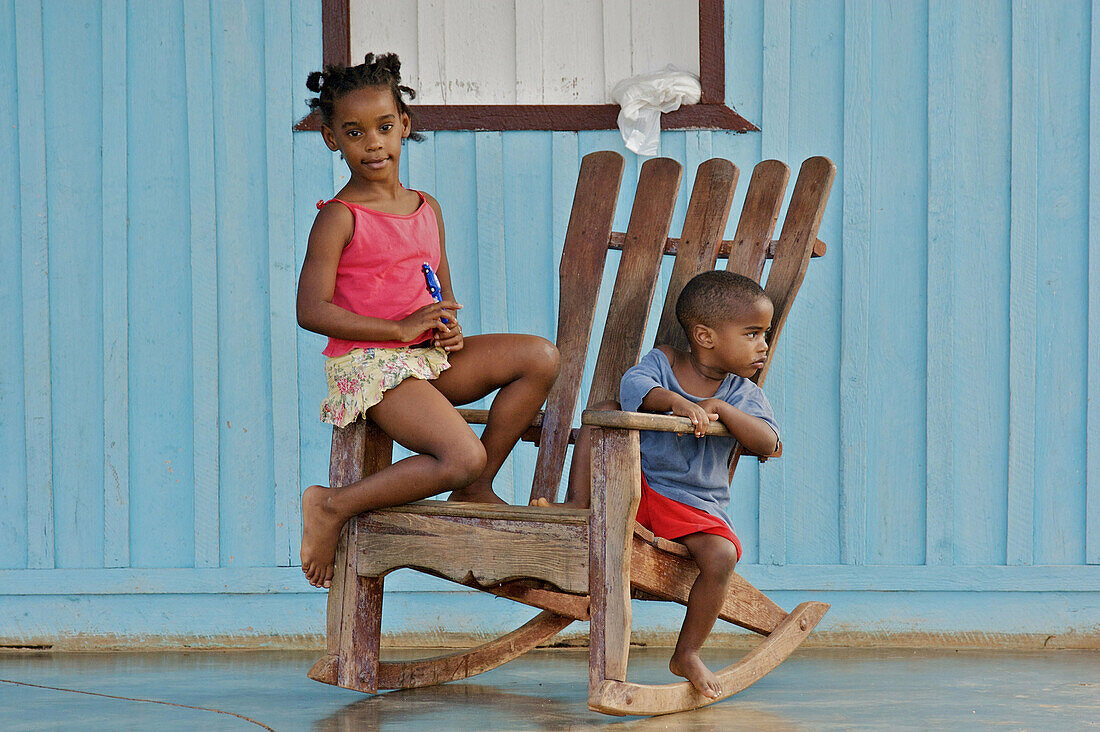 A boy and a girl sitting on a rocking chair on the porch of a house.