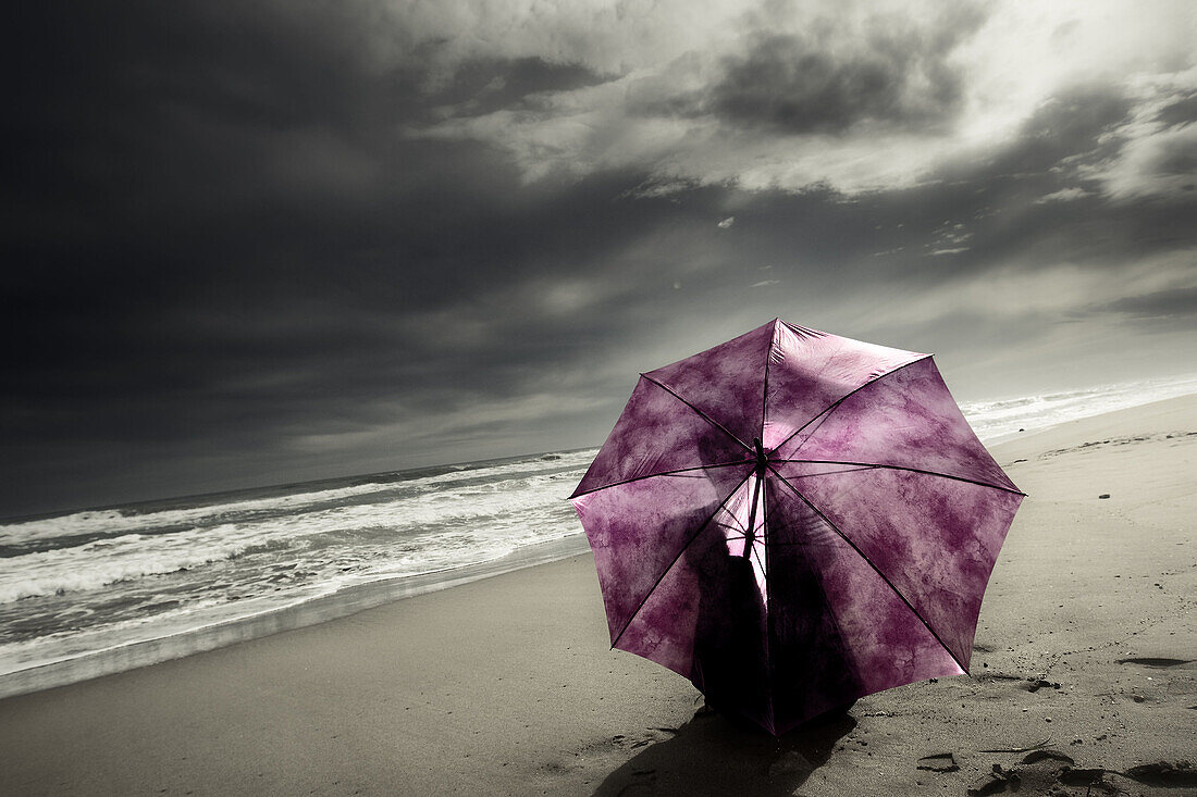 Mujer con paraguas sentada en la playa tras la tormenta.