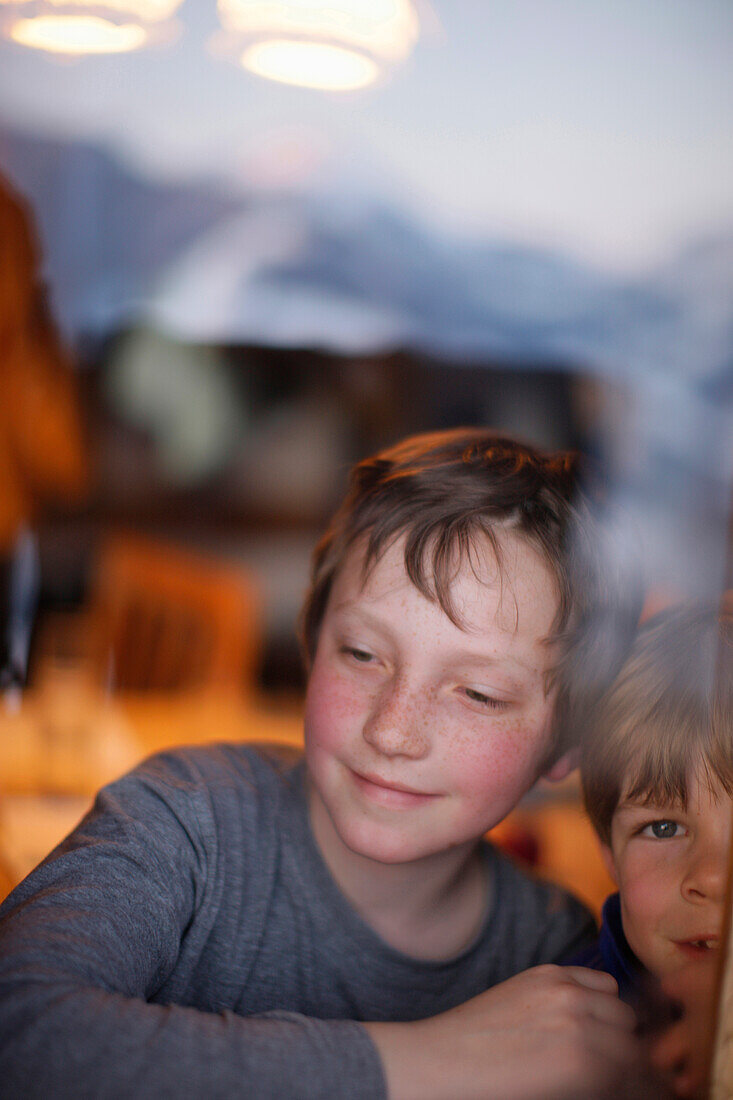 Zwei Jungen blicken aus einem Fenster, Brixen, Tirol, Österreich