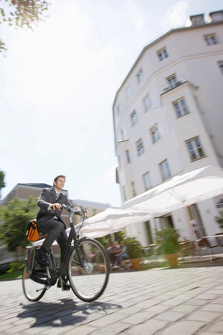 Businessman riding a bicycle over cobblestone pavement, Munich, Bavaria, Germany