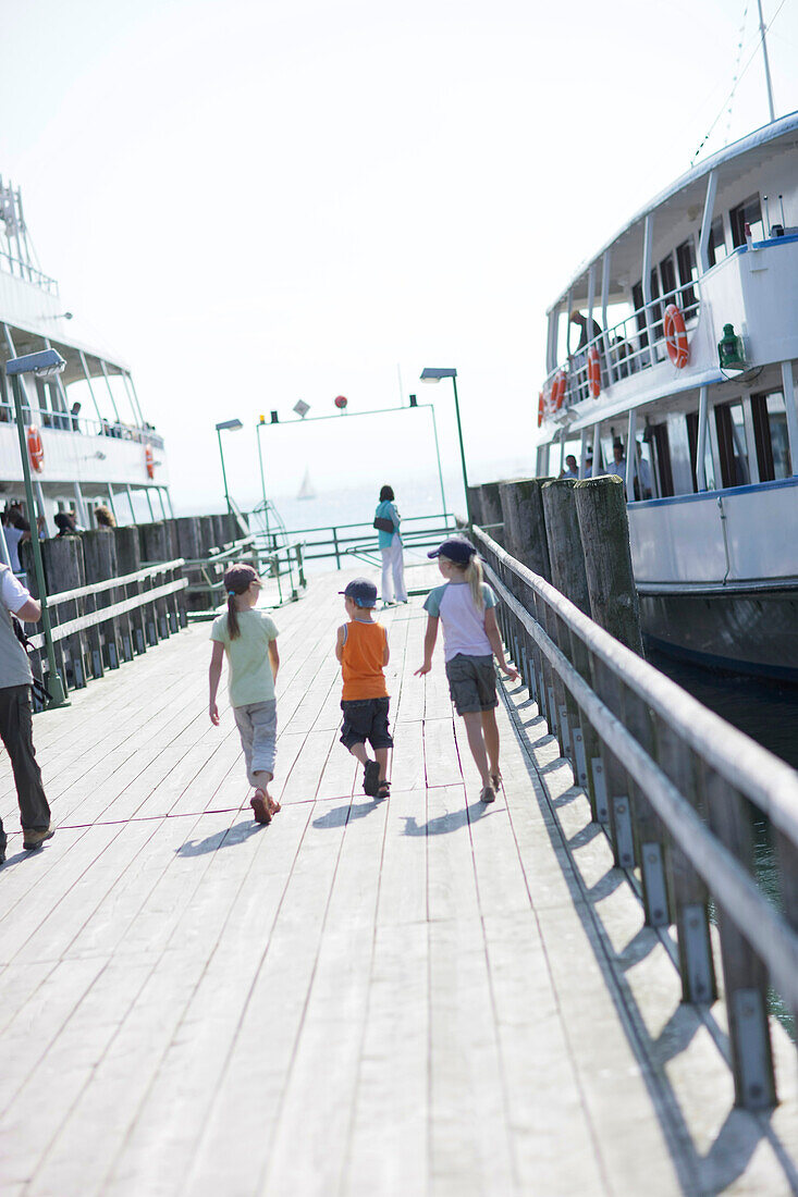 Three children on jetty at Lake Starnberg, Starnberg, Bavaria, Germany