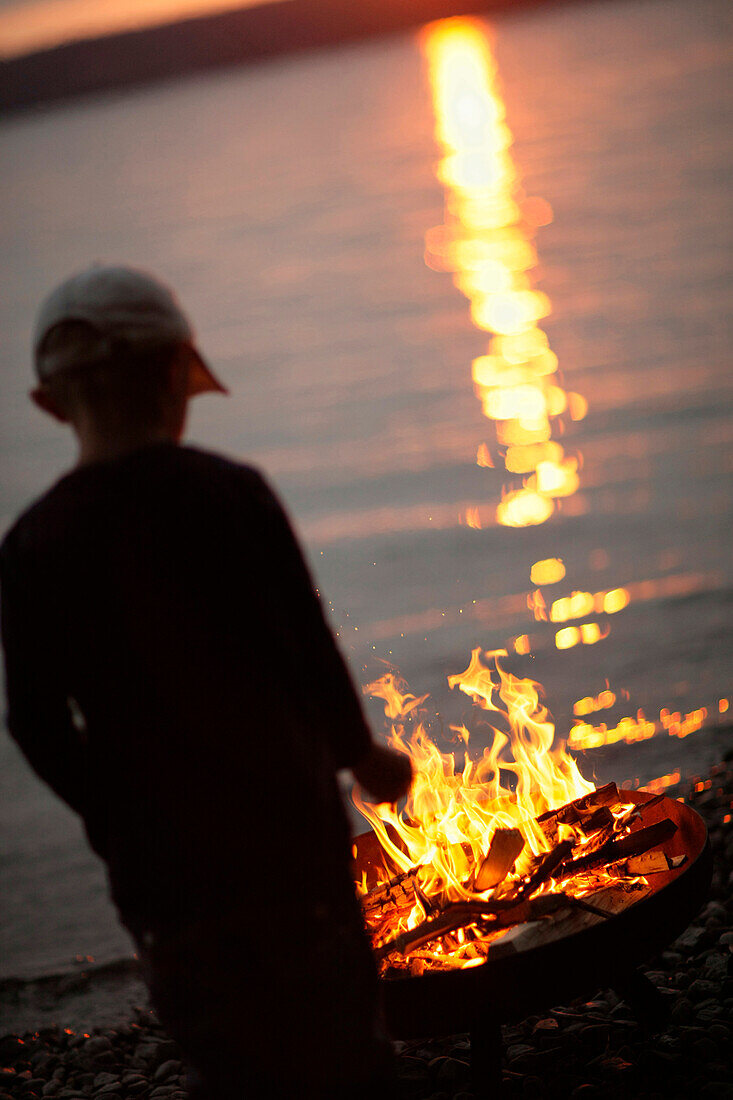 Boy near campfire at lakeside, Lake Starnberg, Bavaria, Germany